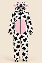 A woman wearing a plush cow-print hooded onesie with pink inner panels and pink ears, seated against a pink studio background. A wicker chair is partly visible on the left, and a circular 'Z Home wear' logo appears in the top right with a code label in the bottom left.