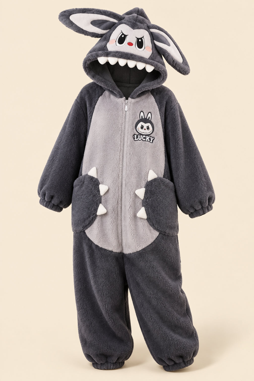 Woman wearing matching dark gray plush bunny onesies in a living room setting. The hoods feature long bunny ears, a cartoon face with white teeth, and paw details on the front.