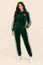 A dark green velour tracksuit set featuring a hooded sweatshirt and matching jogger pants, both with white three-stripes down the sleeves and legs, and a white Adidas logo on the chest.