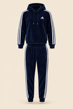 A navy blue Adidas tracksuit laid flat on a white fabric background, featuring a hooded sweatshirt with white three-stripes on the sleeves and a matching pair of jogger pants.