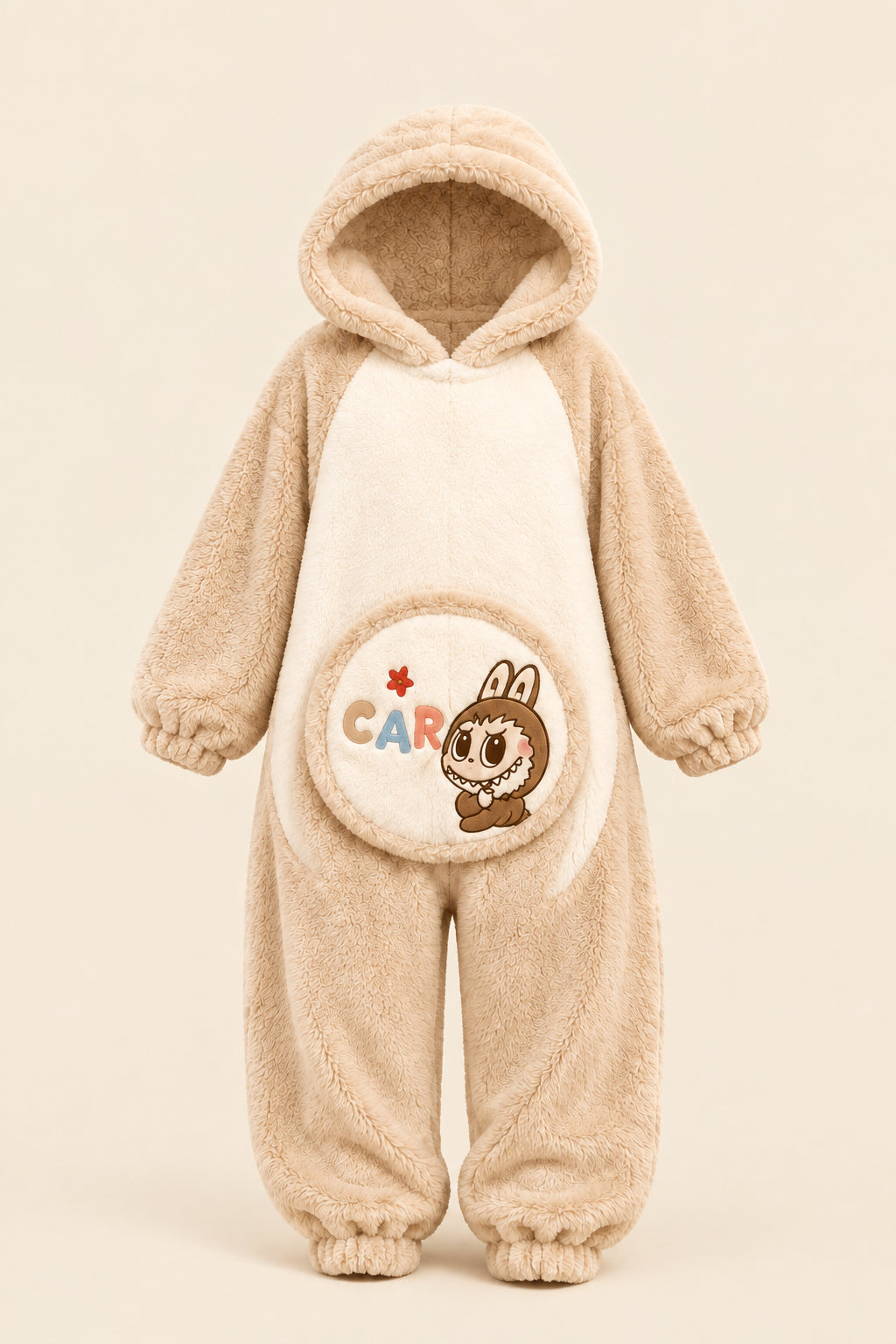 A woman wearing a beige and cream plush hooded pajama set with a cartoon rabbit graphic on the front, sitting on a fluffy rug and making a peace sign. A rabbit plush toy sits on a box to her left, and a brand logo overlay for 'Hesham Lotte' is in the top-left corner.