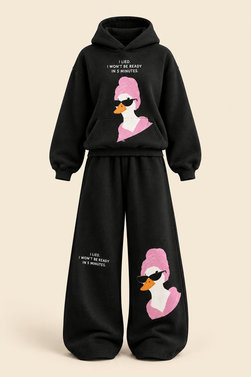 A woman modeling a black two-piece lounge set with a pink and white duck graphic and white text, standing in a room with a dark paneled wall and gray floor. The image includes 'Rose home wear' branding and a pink 'ROSE' banner on the left.