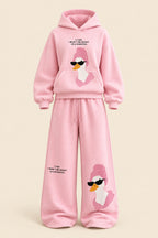 A woman modeling a pink two-piece loungewear set consisting of a pullover hoodie and matching wide-leg sweatpants. The set features a cartoon duck graphic wearing sunglasses on the front of both pieces, with small black text printed on the chest and legs.