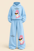A woman modeling a light blue two-piece loungewear set with a cartoon duck graphic and text, standing in an indoor room with a dark paneled wall and gray floor. Brand text 'Rose home wear' and 'ROSE' appear as overlays.