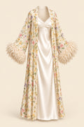A woman models a cream satin slip dress with a matching floral print open-front cardigan featuring feathered bell sleeves, posed in an elegant indoor setting. The brand logo 'Aissaal Lingree' is visible in the top left, with a product code badge in the bottom right.