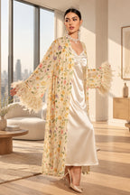 A woman models a cream satin slip dress with a matching floral print open-front cardigan featuring feathered bell sleeves, posed in an elegant indoor setting. The brand logo 'Aissaal Lingree' is visible in the top left, with a product code badge in the bottom right.