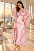 A woman models a pink satin slip dress with a matching sheer floral robe featuring pink feather trim, shown in an elegant indoor setting. The brand name 'Assaial Lingree' is visible in the top left, with two smaller inset images on the left showing front and back views of the dress, and a blue code label on the right.