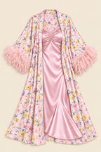 A pink floral robe with fluffy feathered cuffs, layered over a satin pink slip dress, displayed against a solid beige background.