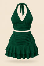 A woman modeling a dark green two-piece halter set with a wrap-style crop top and a ruched ruffled mini skirt, shown in front and back views on a split screen. The image includes a pink 'Diaa shop' logo at the top and contact details at the bottom.