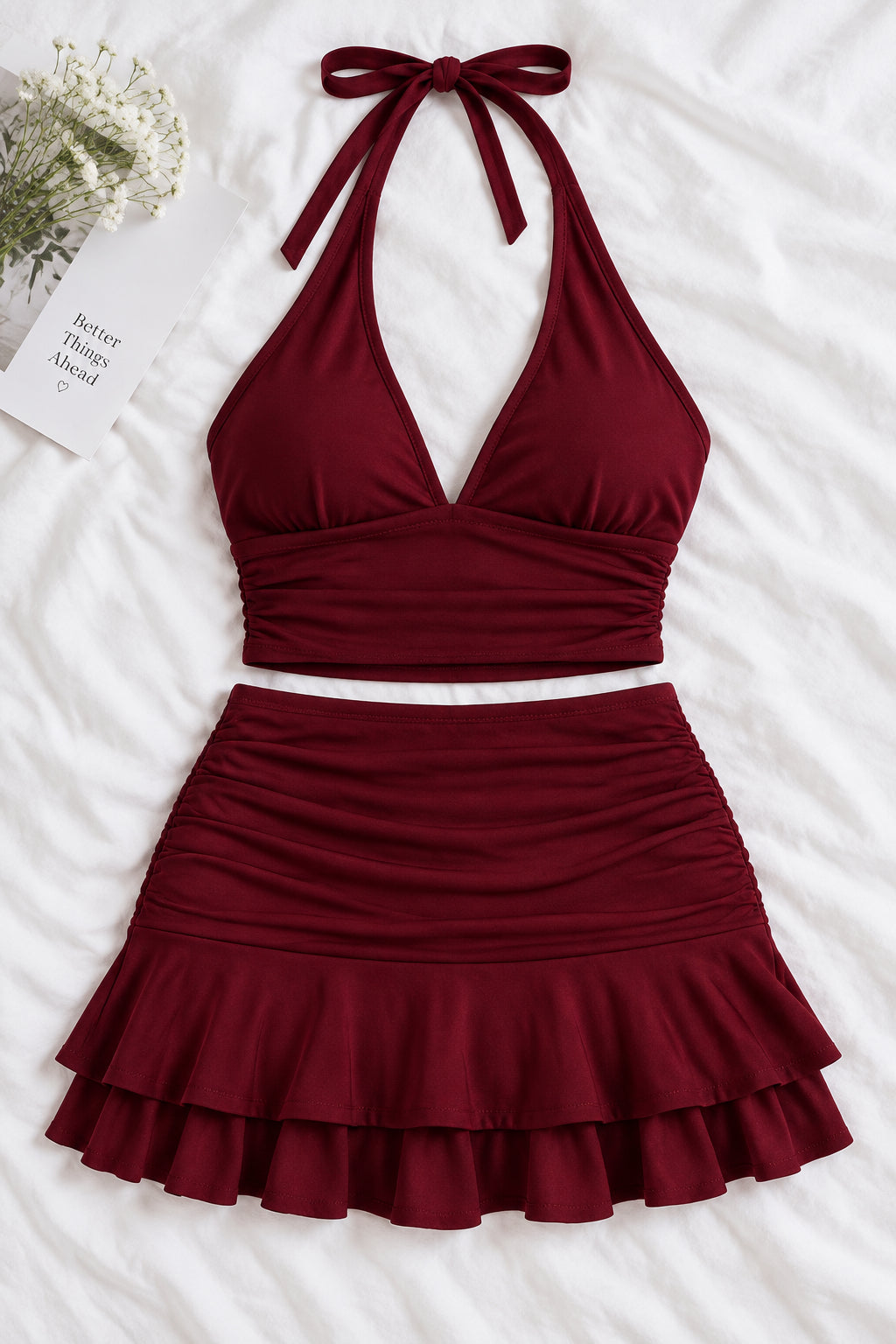 A woman modeling a two-piece burgundy halter crop top and matching ruffled mini skirt, shown in front and back views on a split-screen background. A pink 'Diaa shop' logo appears at the top, with a phone number and code text at the bottom.