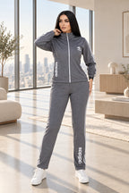 A woman modeling a gray Adidas tracksuit consisting of a zip-up jacket and matching pants, with white Adidas logos on the chest and down the sides. The image has a 'Magic Queen' watermark in the top left, a phone number on the right, and a model badge at the bottom.