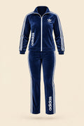 A woman modeling a navy blue Adidas tracksuit with white stripes and logos, standing outdoors on a paved walkway with trees in the background. The image includes 'Magic Queen' branding and contact details.