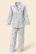 A person wearing a light blue pajama set with a cartoon character print, taking a mirror selfie in an indoor room. The pajamas feature a long-sleeve button-up top and matching pants with a playful multicolor character pattern.