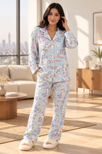 A person wearing a light blue pajama set with a cartoon character print, taking a mirror selfie in an indoor room. The pajamas feature a long-sleeve button-up top and matching pants with a playful multicolor character pattern.